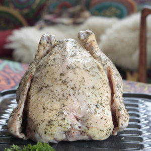 Organic whole chicken raw with herbs on a roasting pan