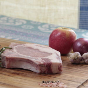 Pasture-Raised Pork Chop on a cutting board with apples and garlic