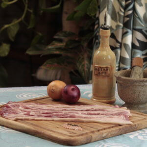 pasture-raised pork belly slices on a cutting board with apples and a bottle of cooking oil